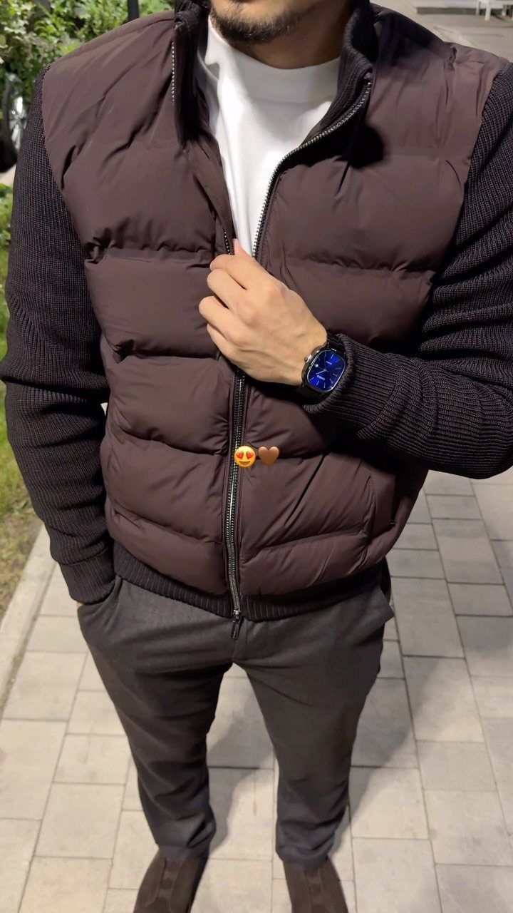 Man wearing a brown puffer vest over a brown sweater and grey trousers.