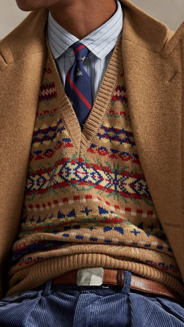 Brown patterned sweater vest with blue corduroy pants and camel overcoat.