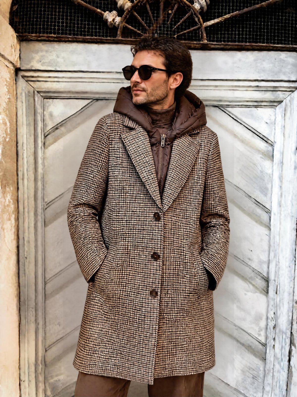 Man wearing a brown quilted vest and a brown plaid overcoat with sunglasses.