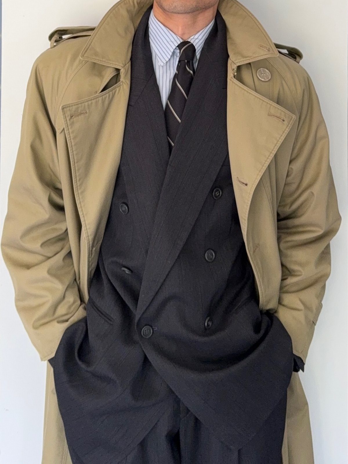 Man wearing a camel trench coat over a charcoal striped double-breasted suit and tie.