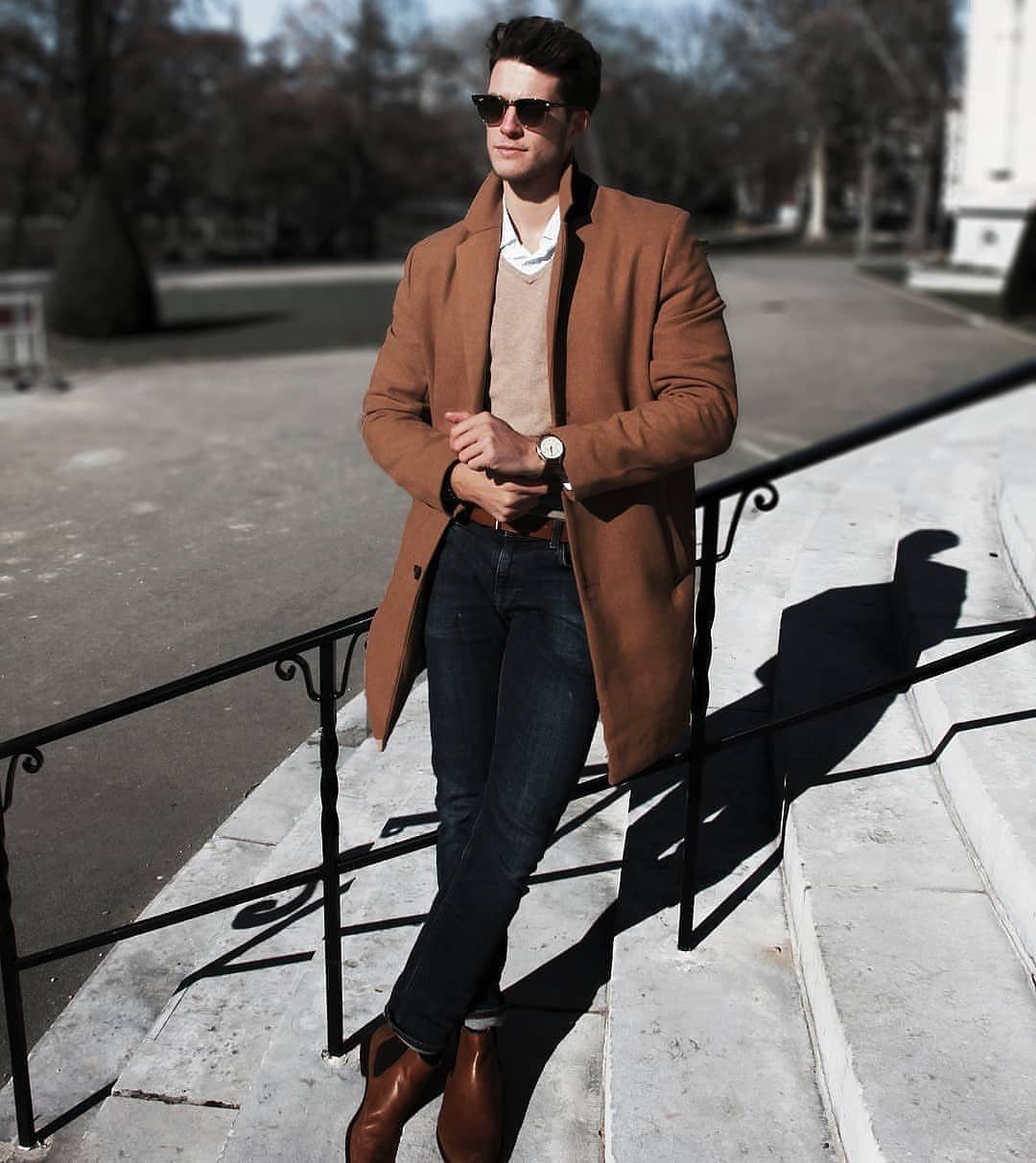 Man in camel coat and navy jeans standing on white stone outdoor steps.