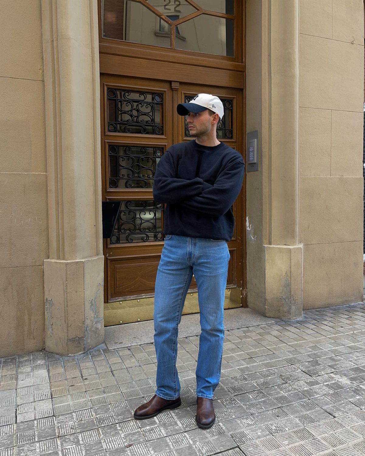 Man wearing a black sweater and light blue straight-leg jeans standing outdoors.