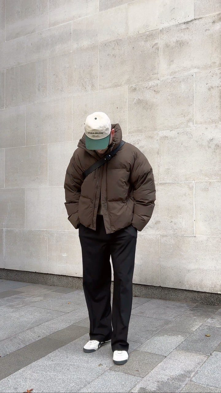 Person wearing a brown puffer jacket, black pants, and a beige cap.