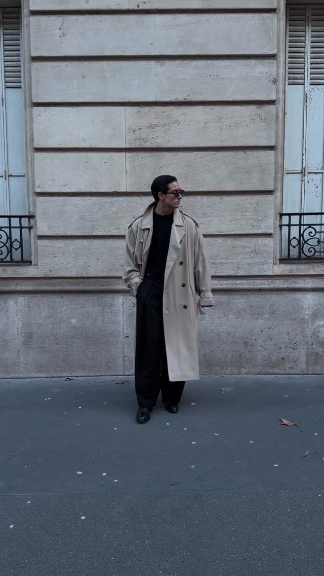 Person wearing a long beige trench coat and black outfit on a city street.