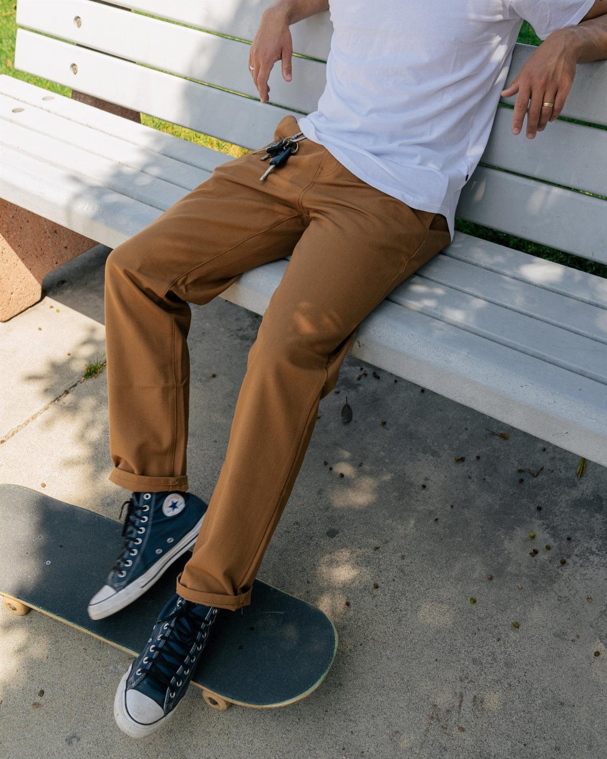 Person wearing brown work pants and navy sneakers sitting on a white bench.