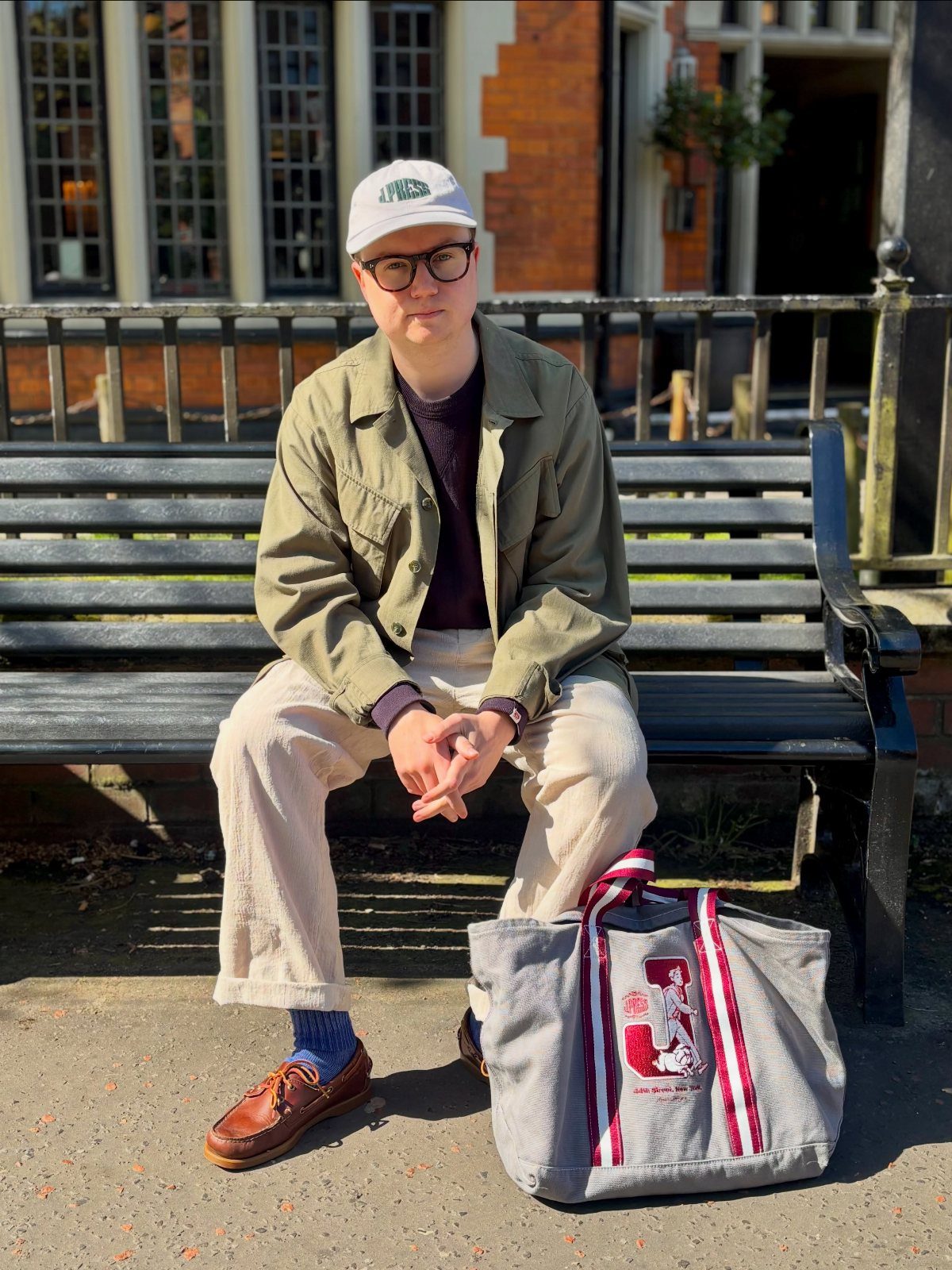 Person in casual spring attire wearing brown leather boat shoes sitting on a bench