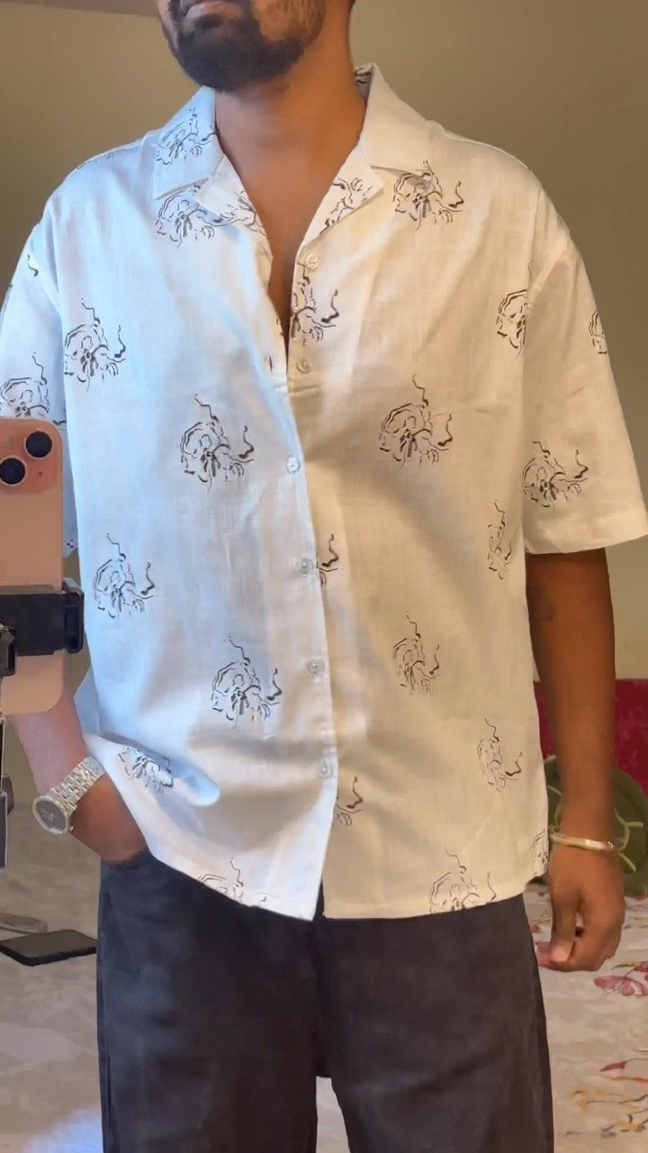 Man wearing a white short-sleeved button-down shirt with brown animal prints and dark trousers.