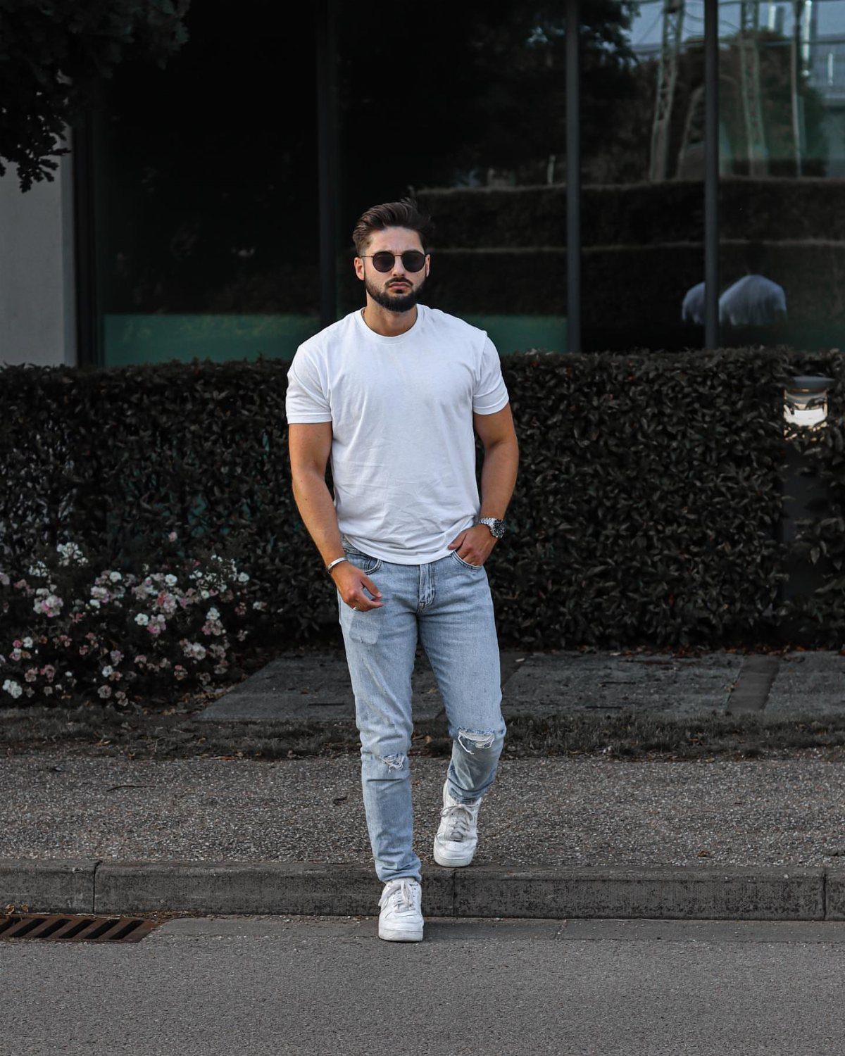 Man wearing a classic white tee, light blue jeans, and white sneakers outdoors.