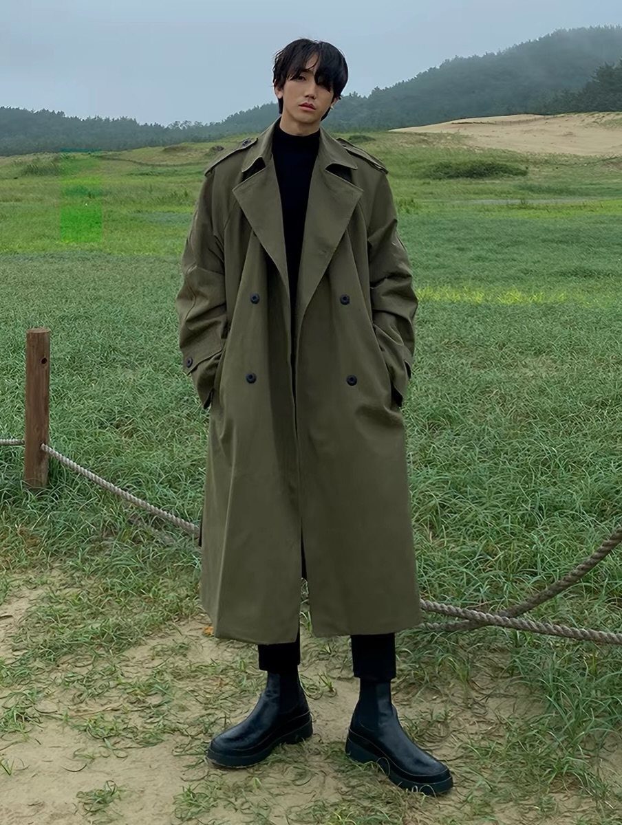 Person wearing an olive green trench coat and black boots in a grassy field