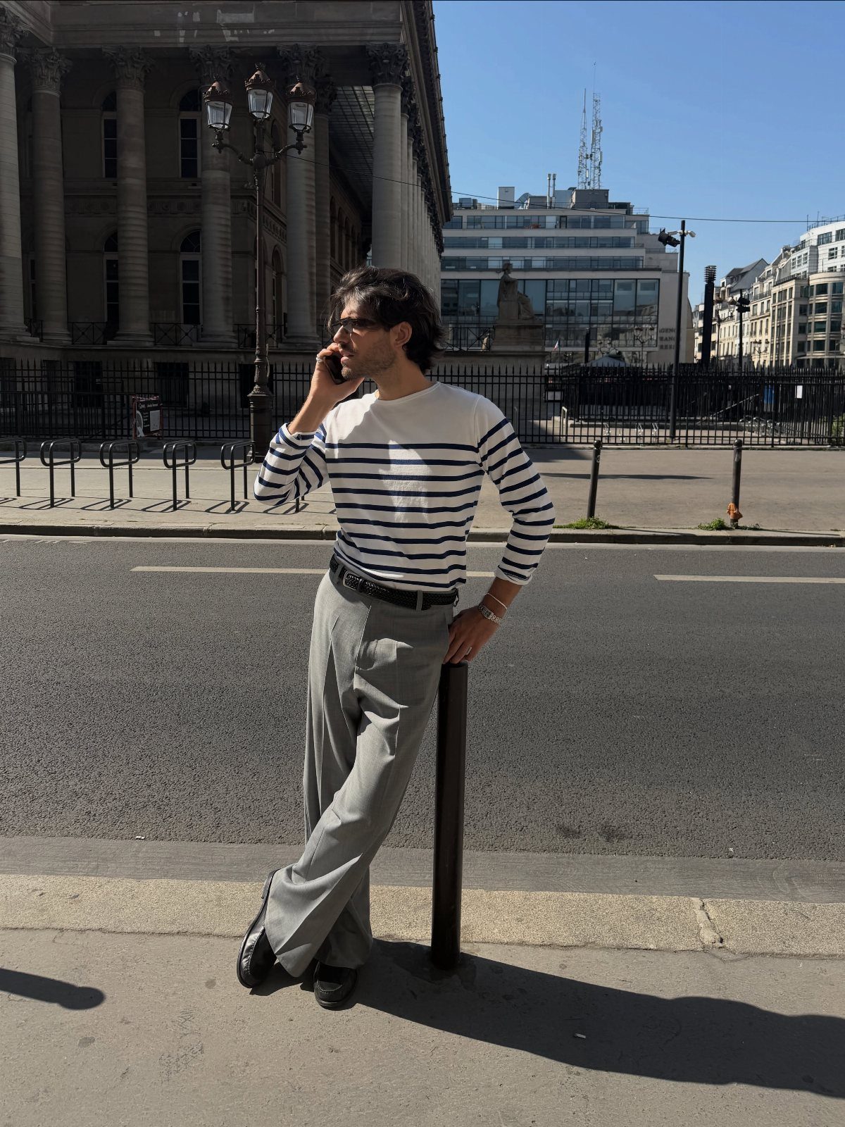 Man in striped Breton top and grey trousers talking on phone in city