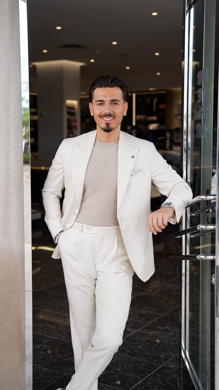 Man wearing a cream lightweight suit and beige t-shirt standing in a doorway.