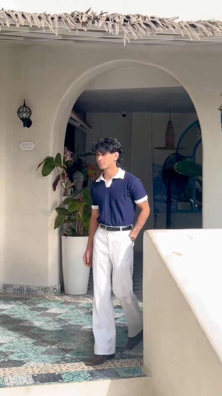 Man wearing a navy blue polo shirt and white trousers in an arched doorway.
