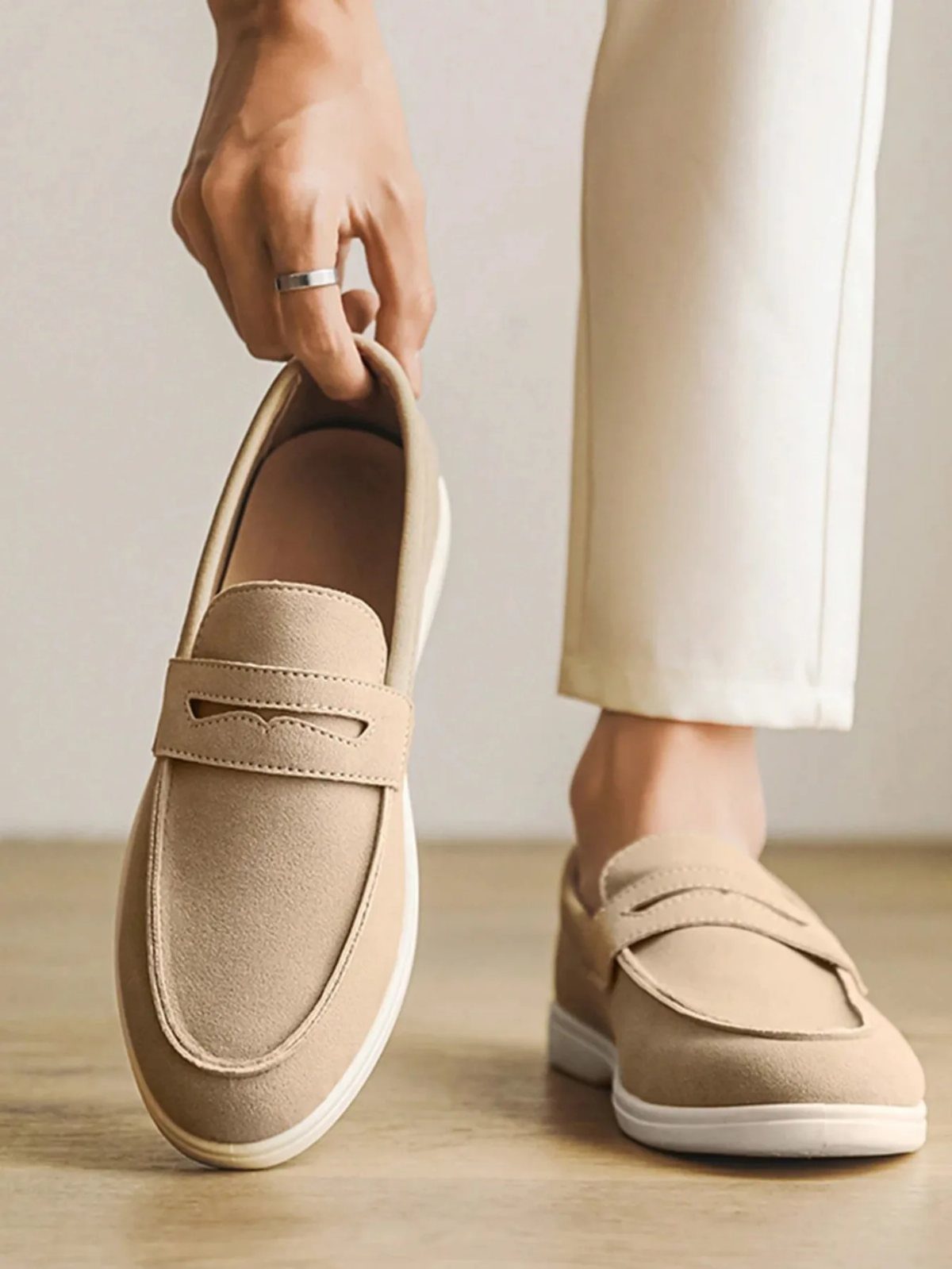 Tan suede loafers paired with cream trousers on a light wooden floor.