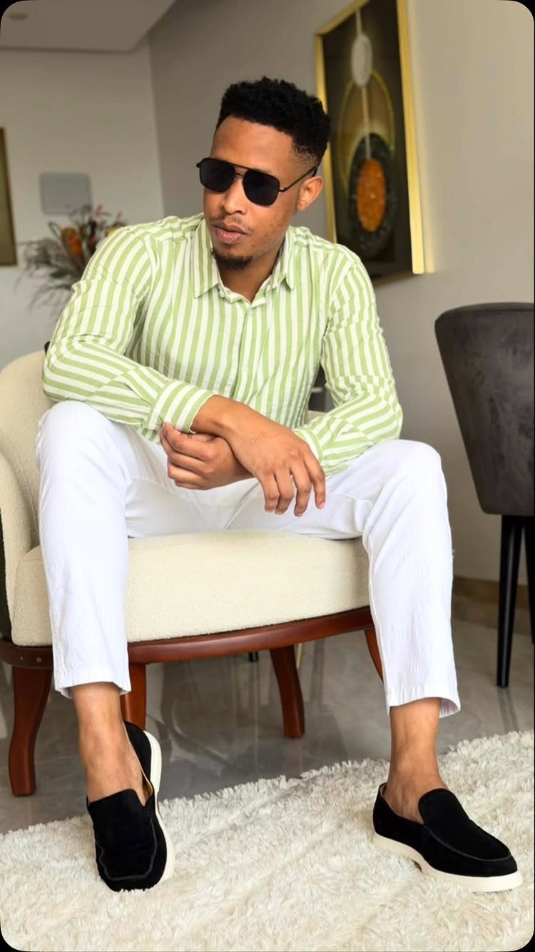 Man in green striped shirt and white trousers sitting on a chair.