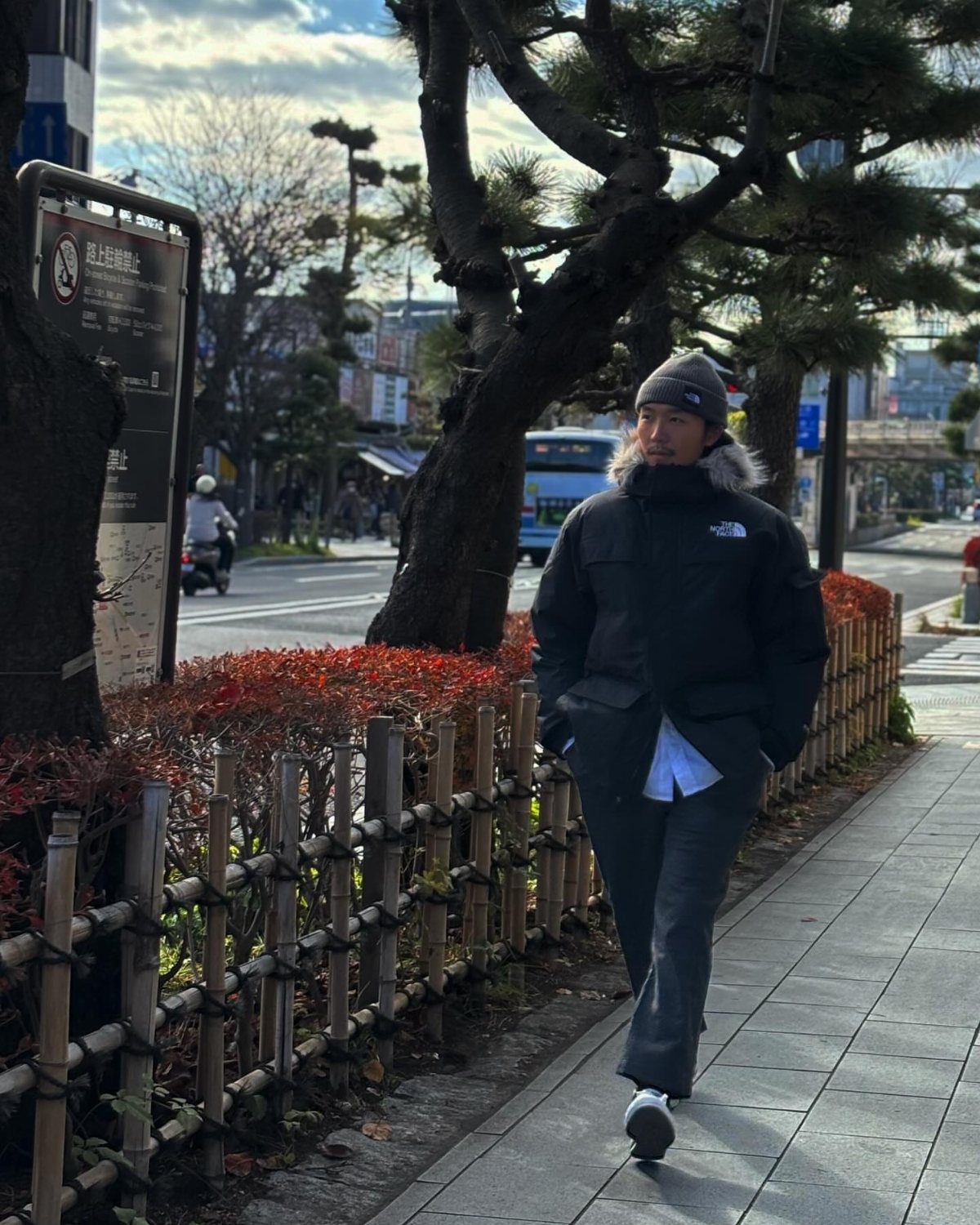 Man walking on a city sidewalk wearing a black hooded winter parka and beanie.