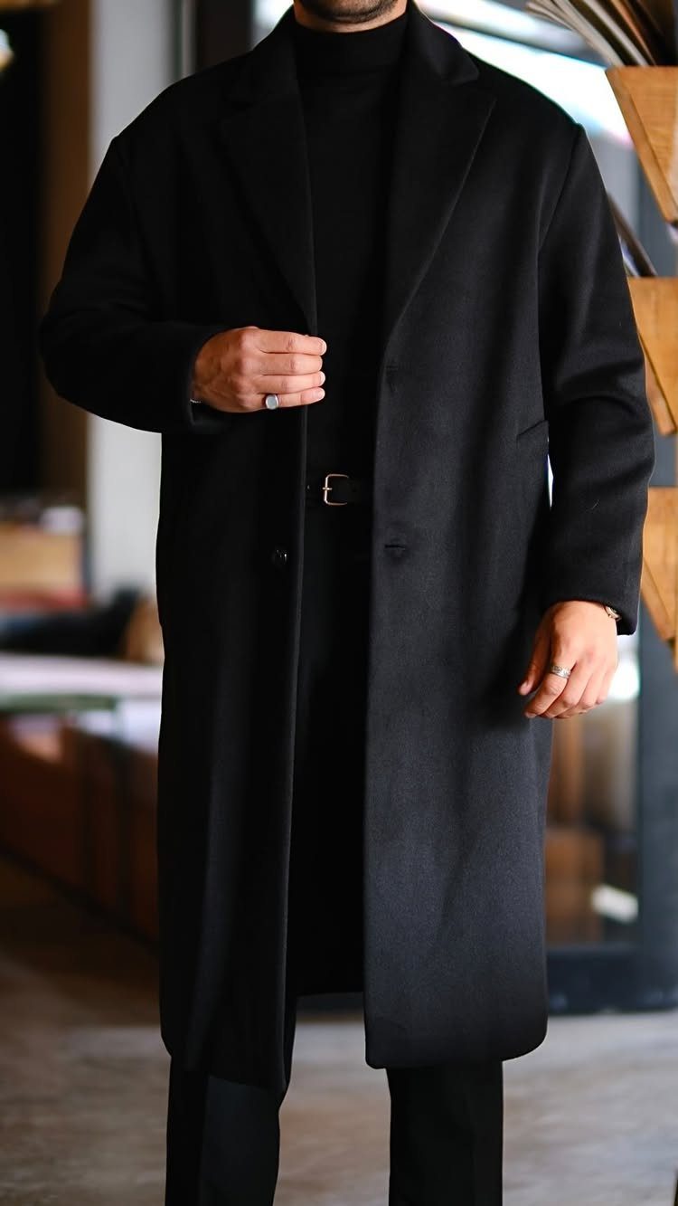 Man wearing a long black wool overcoat and black turtleneck in indoor setting
