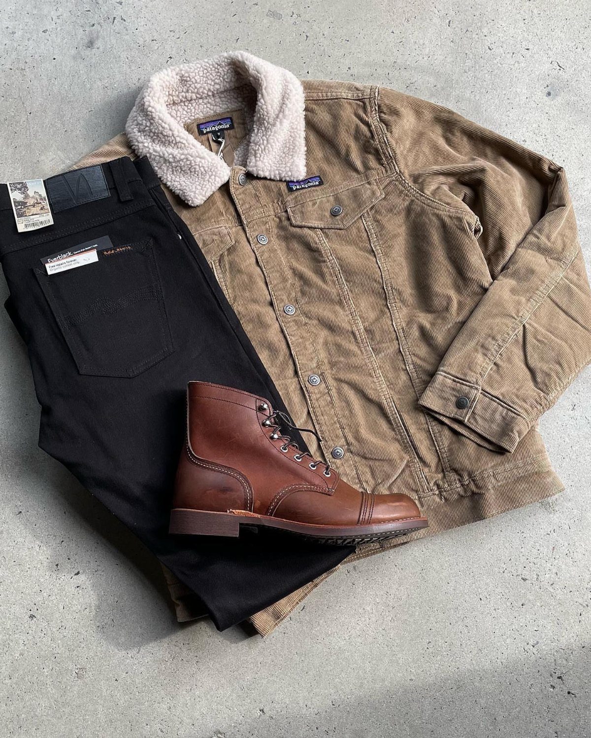 Tan corduroy jacket with sherpa collar, black pants, and brown leather boot.