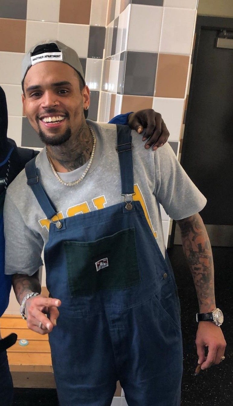 Man wearing navy blue denim overalls over a grey t-shirt and grey cap.