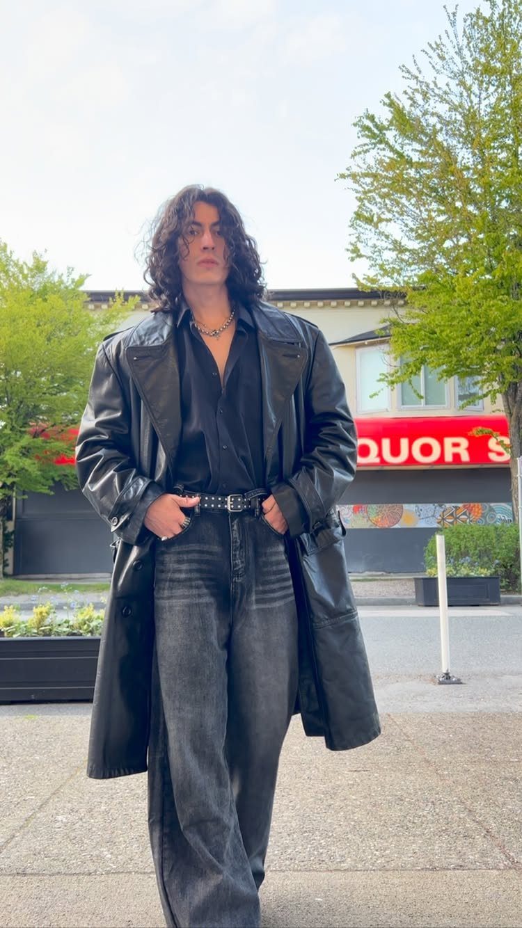 Person wearing a long black leather coat and wide-leg grey denim jeans outdoors.