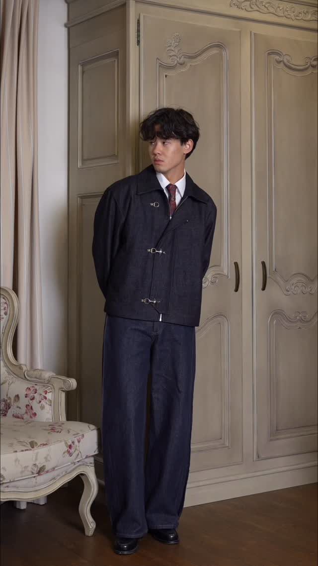 Man wearing a navy toggle coat and wide-leg blue jeans standing by a wardrobe
