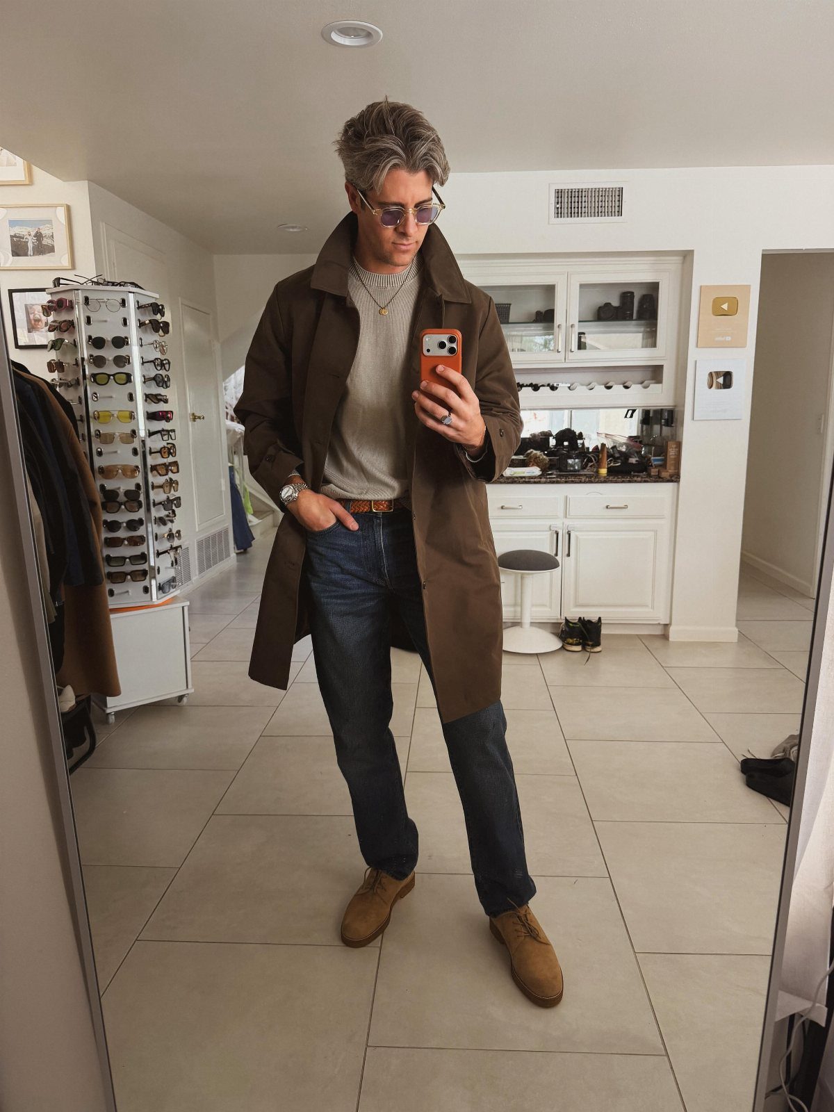 Man in brown coat and dark blue jeans posing for a mirror selfie.