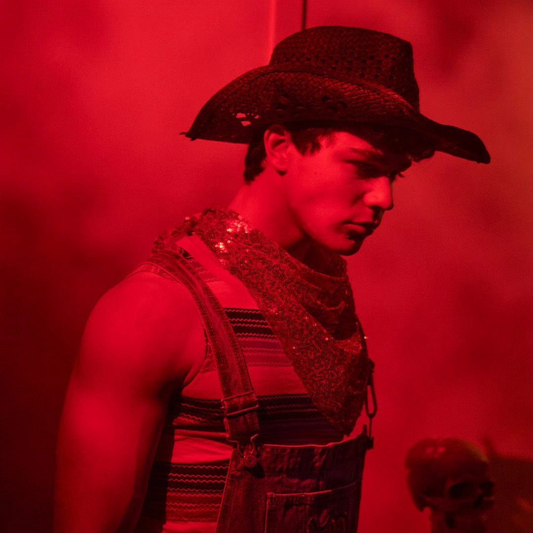 Man in cowboy hat and denim overalls under dramatic red lighting