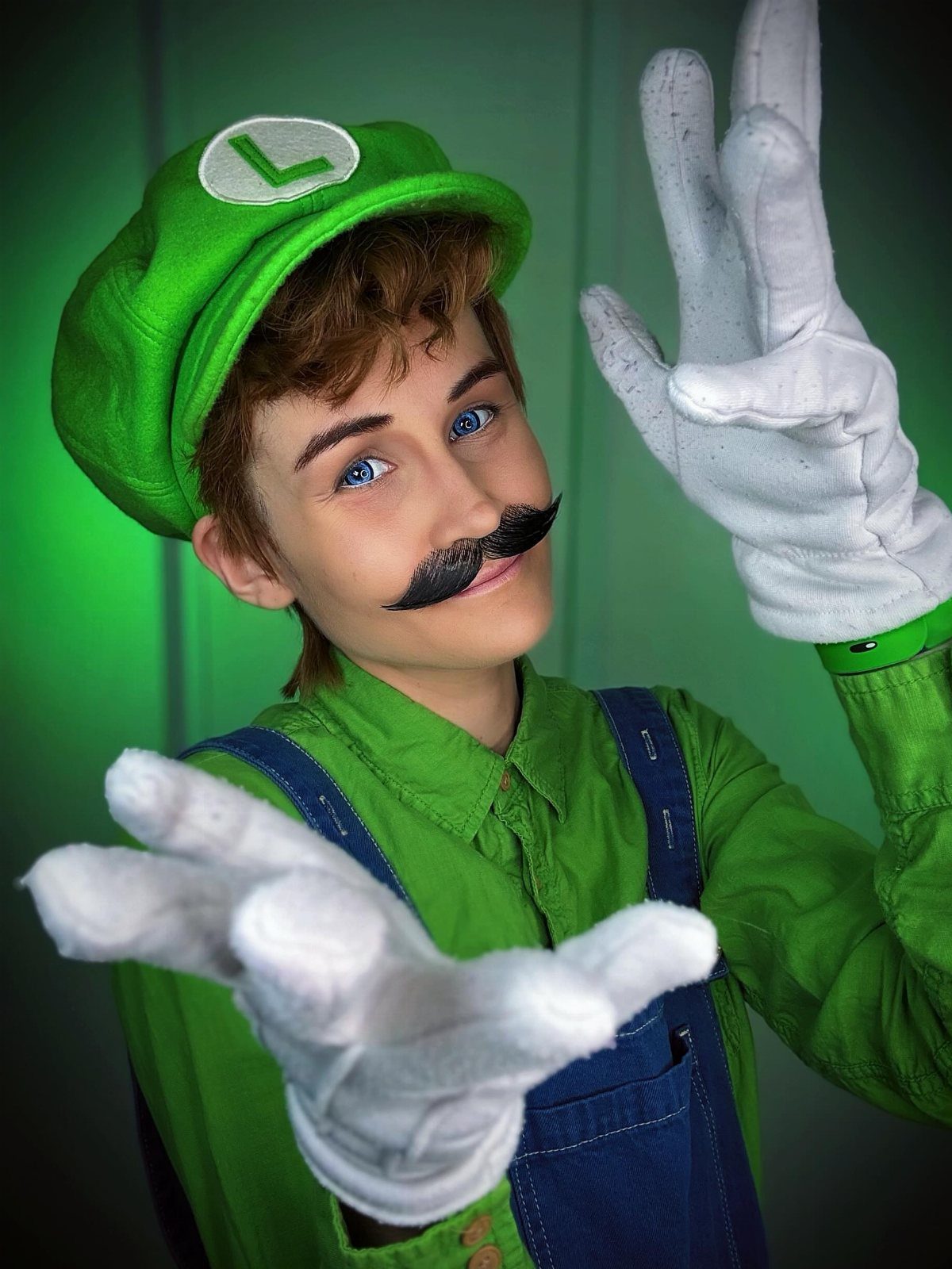 Person dressed as Luigi wearing a green cap, green shirt, and blue overalls.