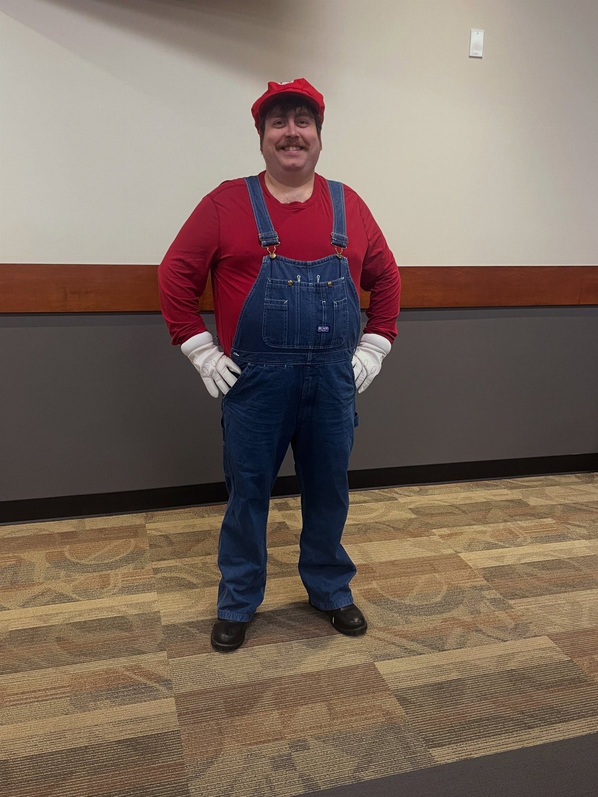 Man dressed as Mario wearing a red shirt, blue overalls, and red cap.