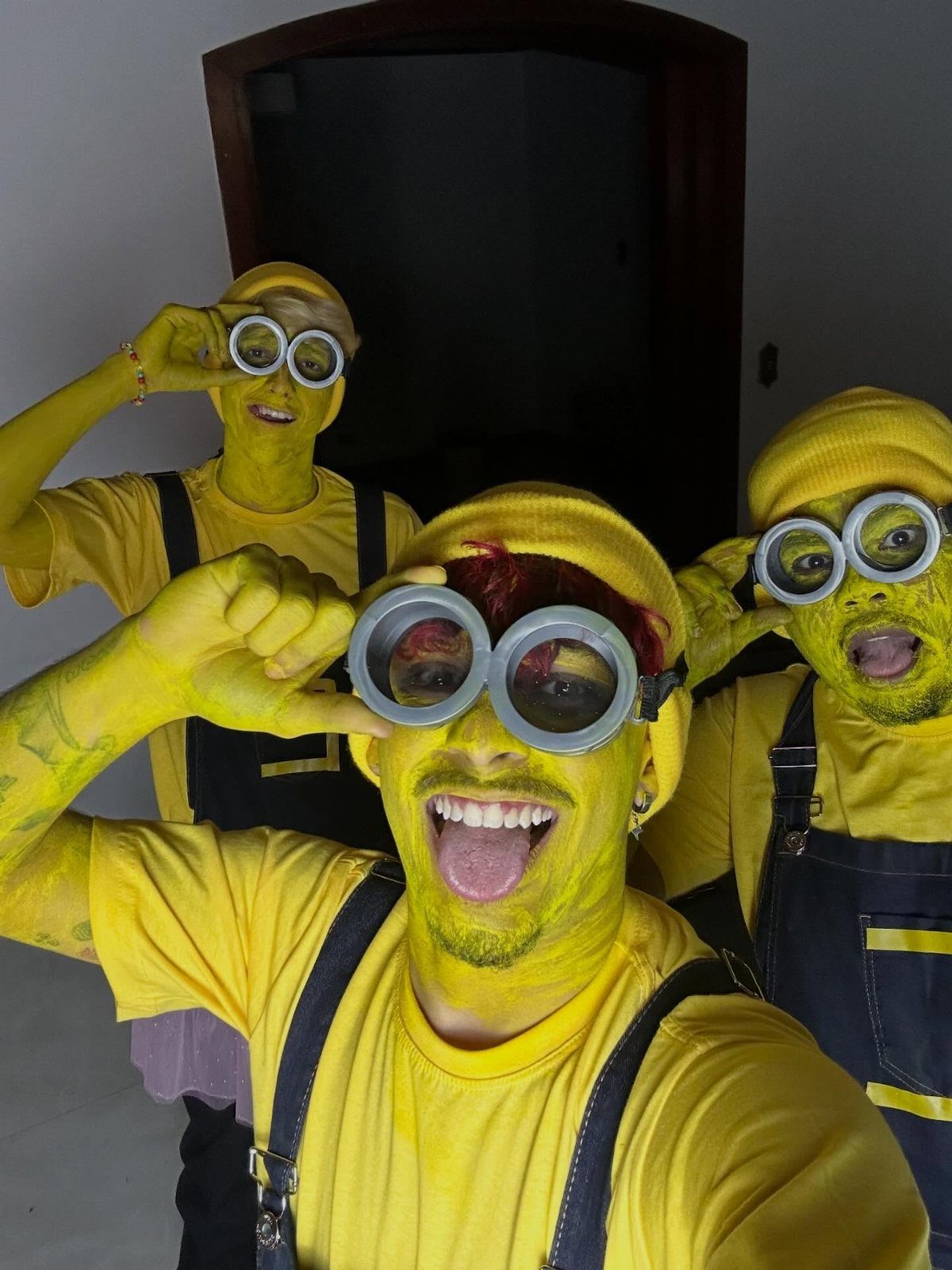 Three people dressed as Minions with yellow skin, goggles, and denim overalls.
