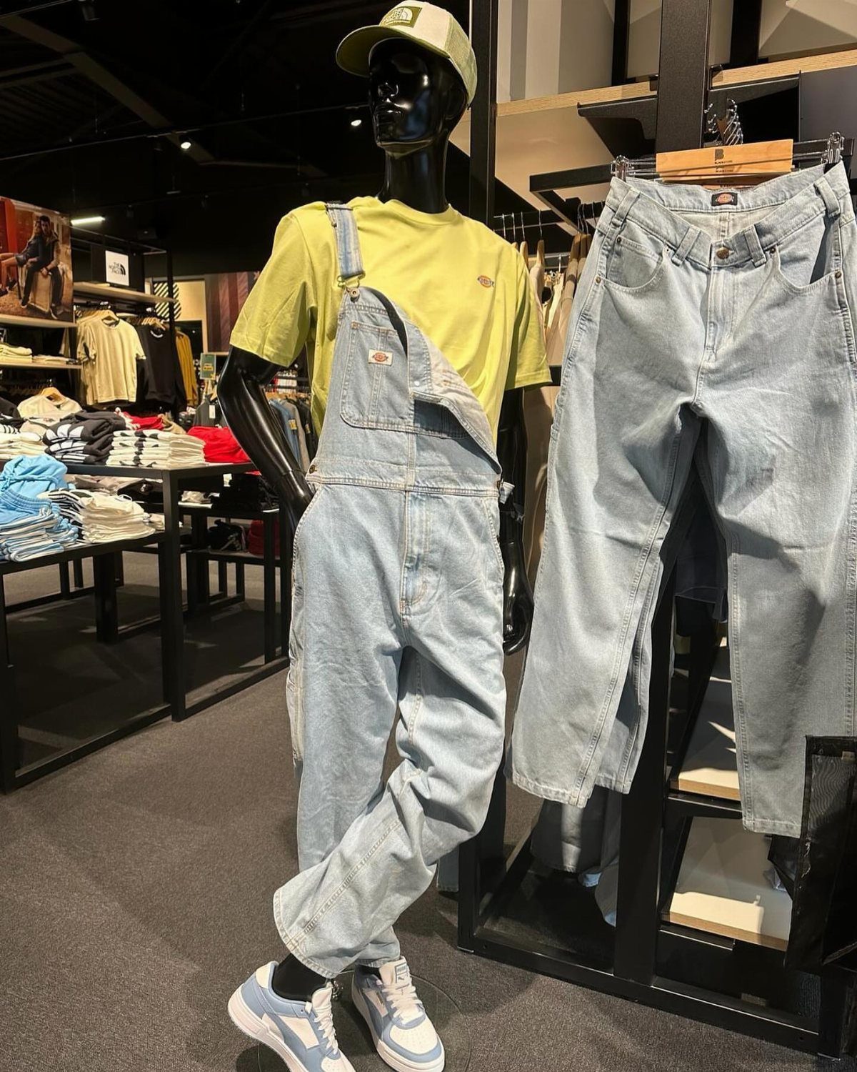 Mannequin wearing light blue denim overalls with a lime green t-shirt and cap.