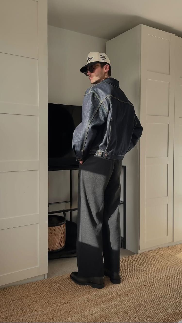 Person wearing a cropped denim jacket and wide-leg grey trousers standing indoors.