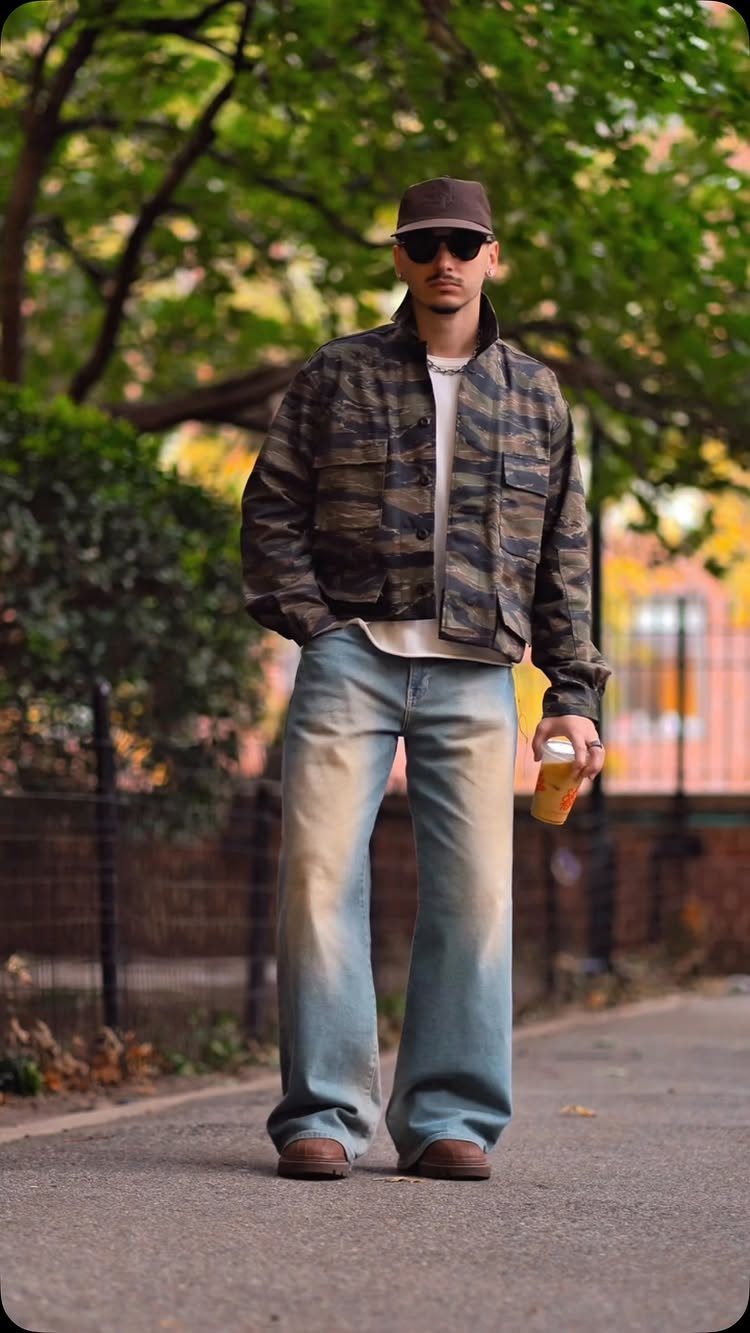 Man wearing a cropped camouflage utility jacket and wide-leg light-wash denim jeans.