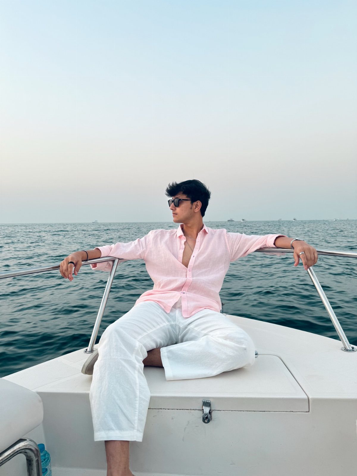 Man in pink shirt and white trousers sitting on a boat at sea.