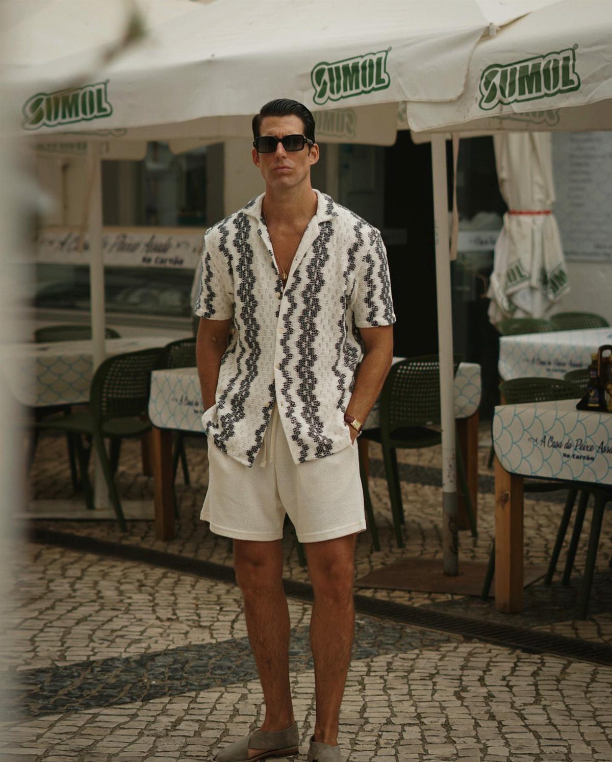 Man wearing a patterned white Didcot shirt and white shorts on a cobblestone street