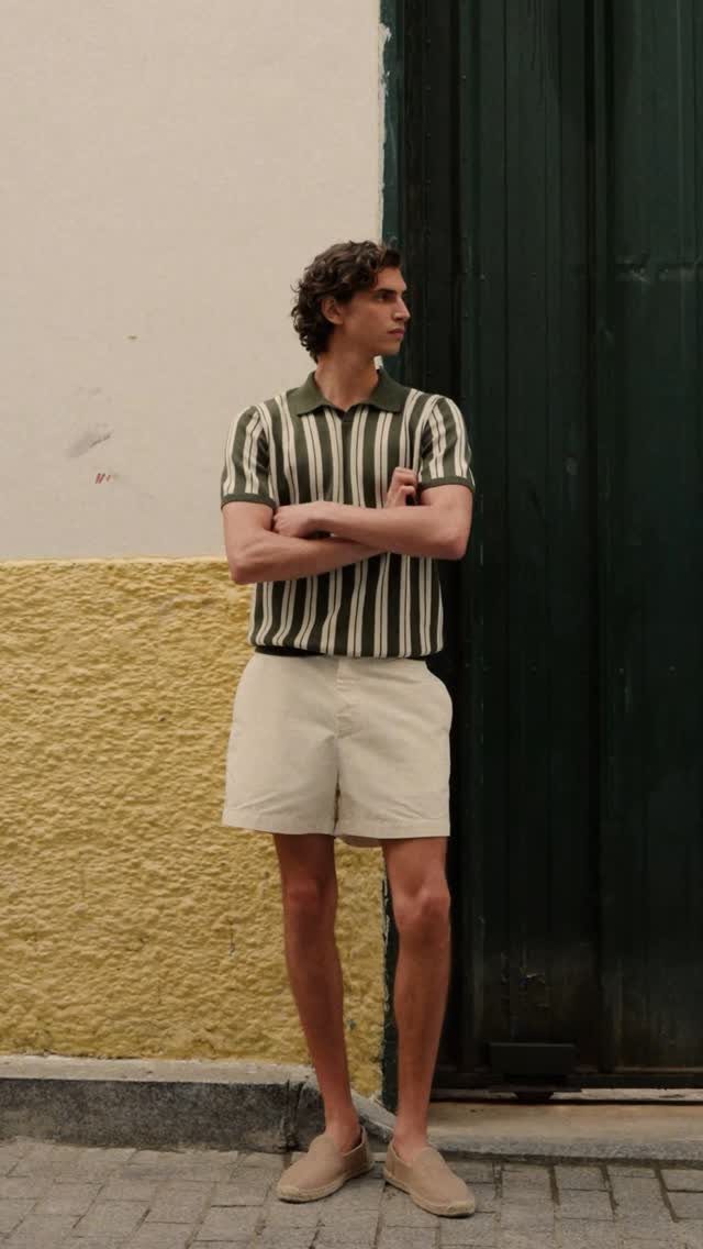 Man wearing a green striped polo shirt and off-white shorts standing outdoors.