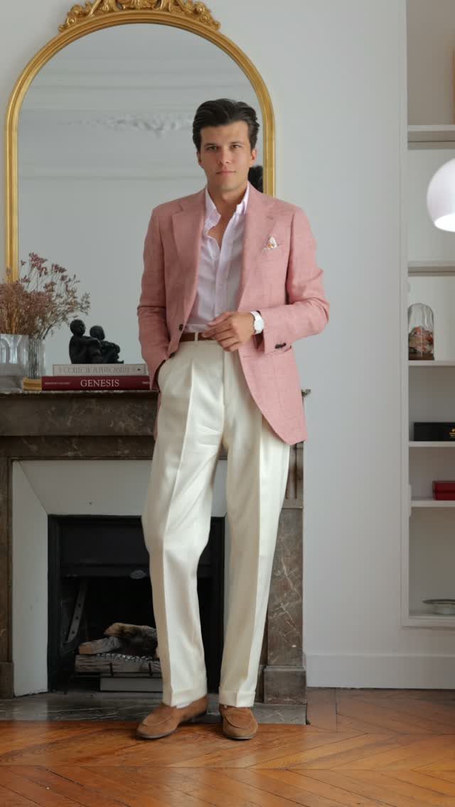 Man wearing a pink blazer and cream trousers standing in a classic interior.
