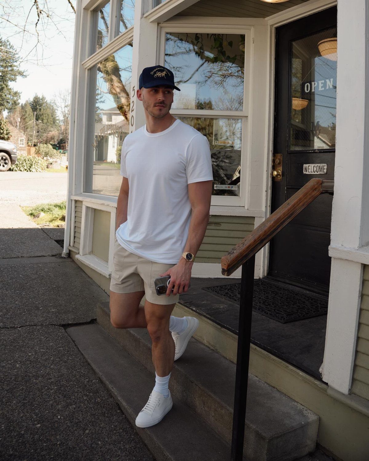 Man wearing white t-shirt and beige shorts standing outside a storefront