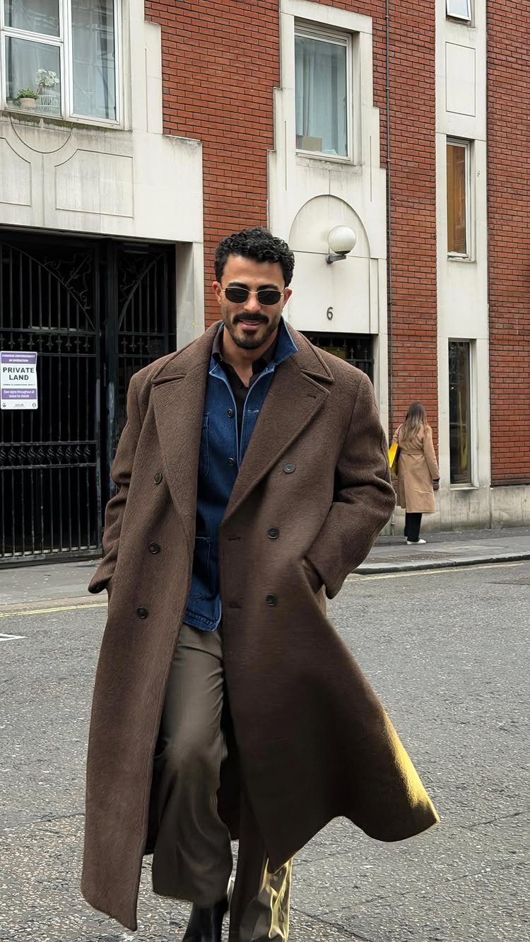 Man wearing a dark brown trench coat, blue shirt, and olive trousers on street