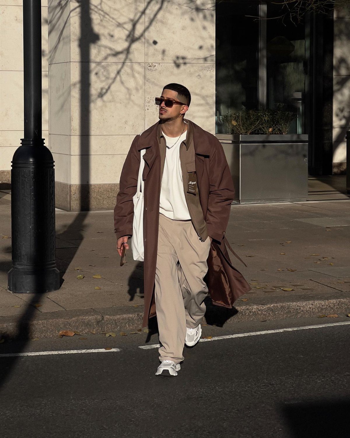 Man wearing a dark brown trench coat and beige chinos walking on a sidewalk