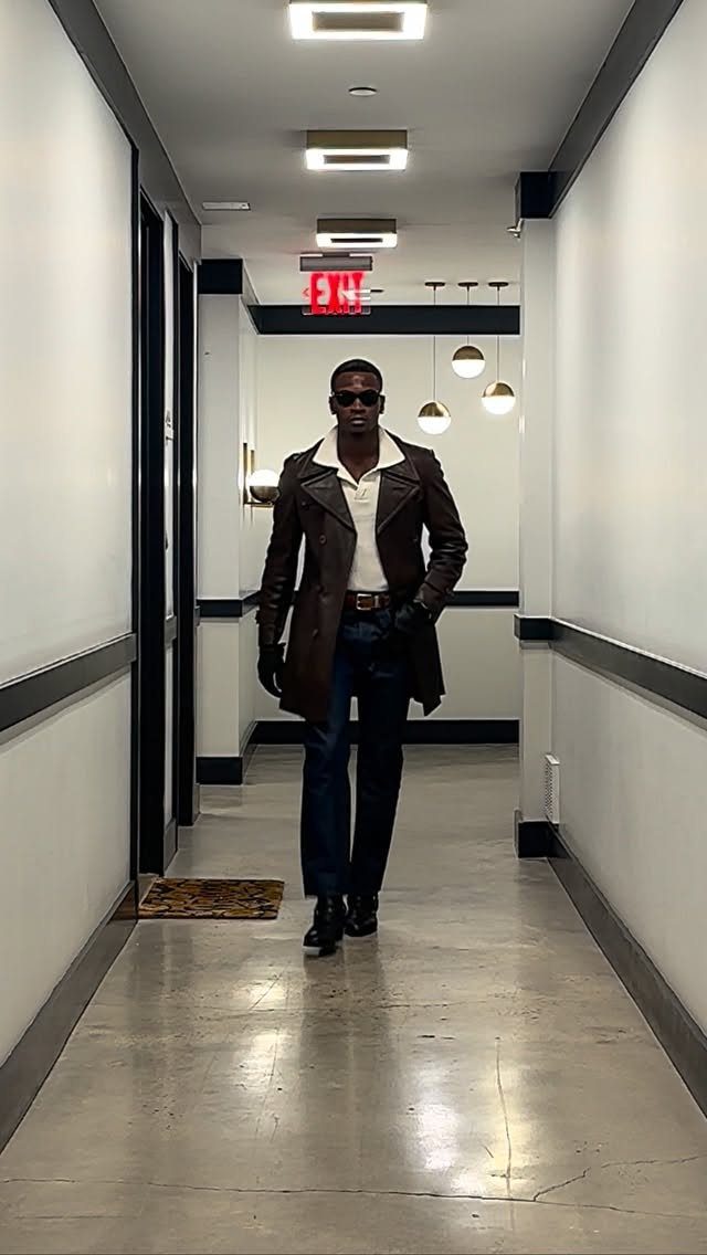 Man in a dark brown leather trench coat and navy blue trousers in a hallway
