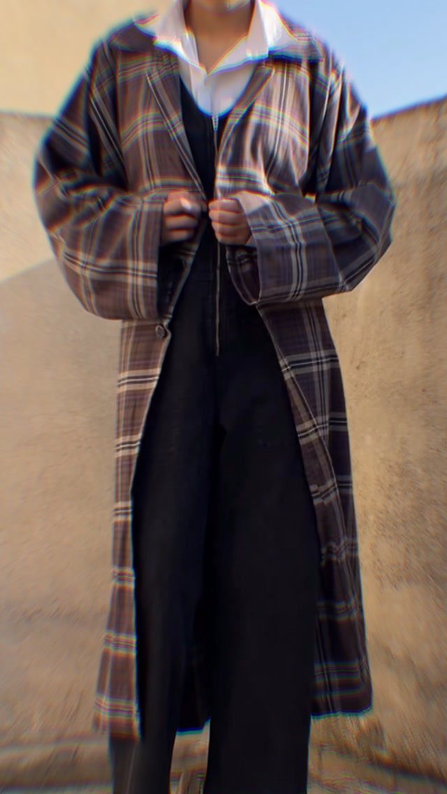 Person wearing a dark brown plaid trench coat with black trousers and white shirt.