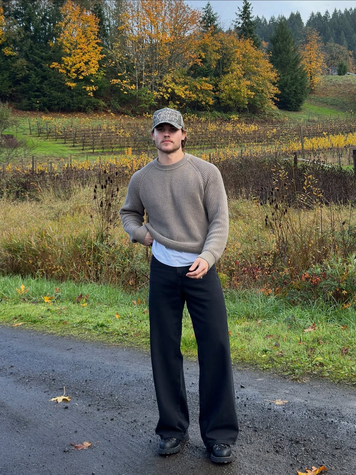 Man wearing a brown knit sweater and black wide-leg trousers in autumn landscape