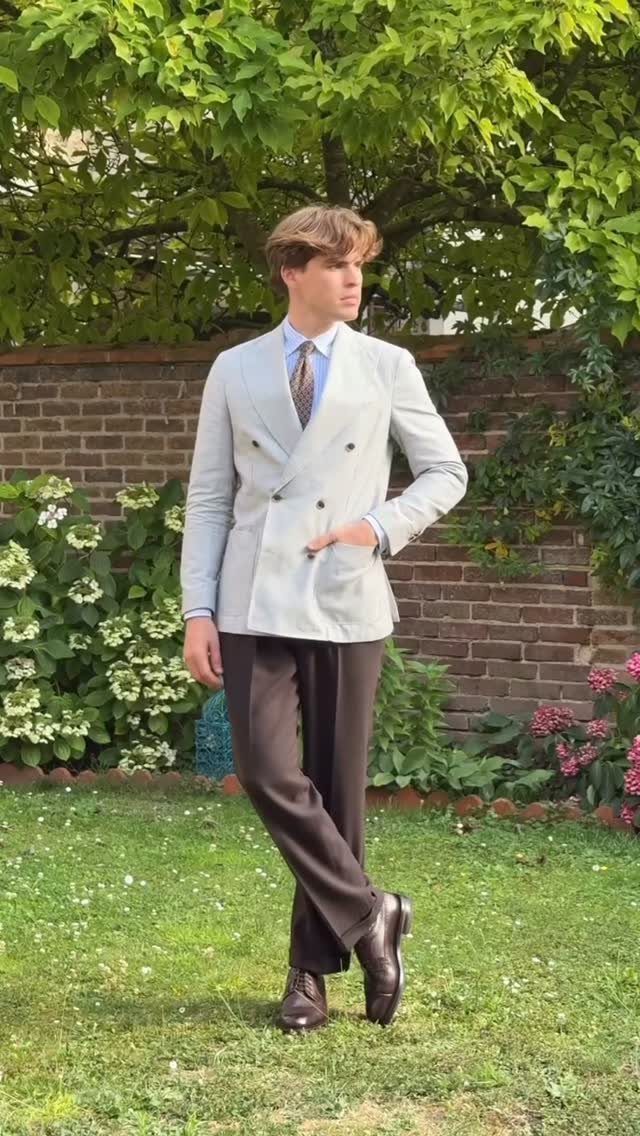 Man in a light grey blazer and dark brown trousers standing in a garden