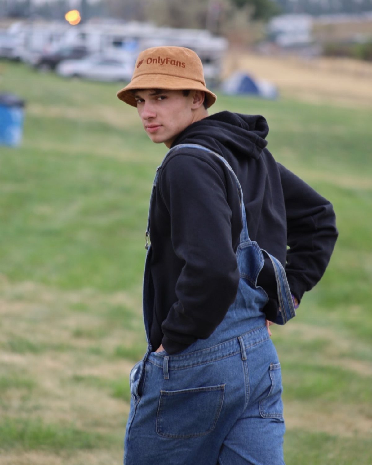 Man in blue denim overalls and black hoodie wearing a brown bucket hat.