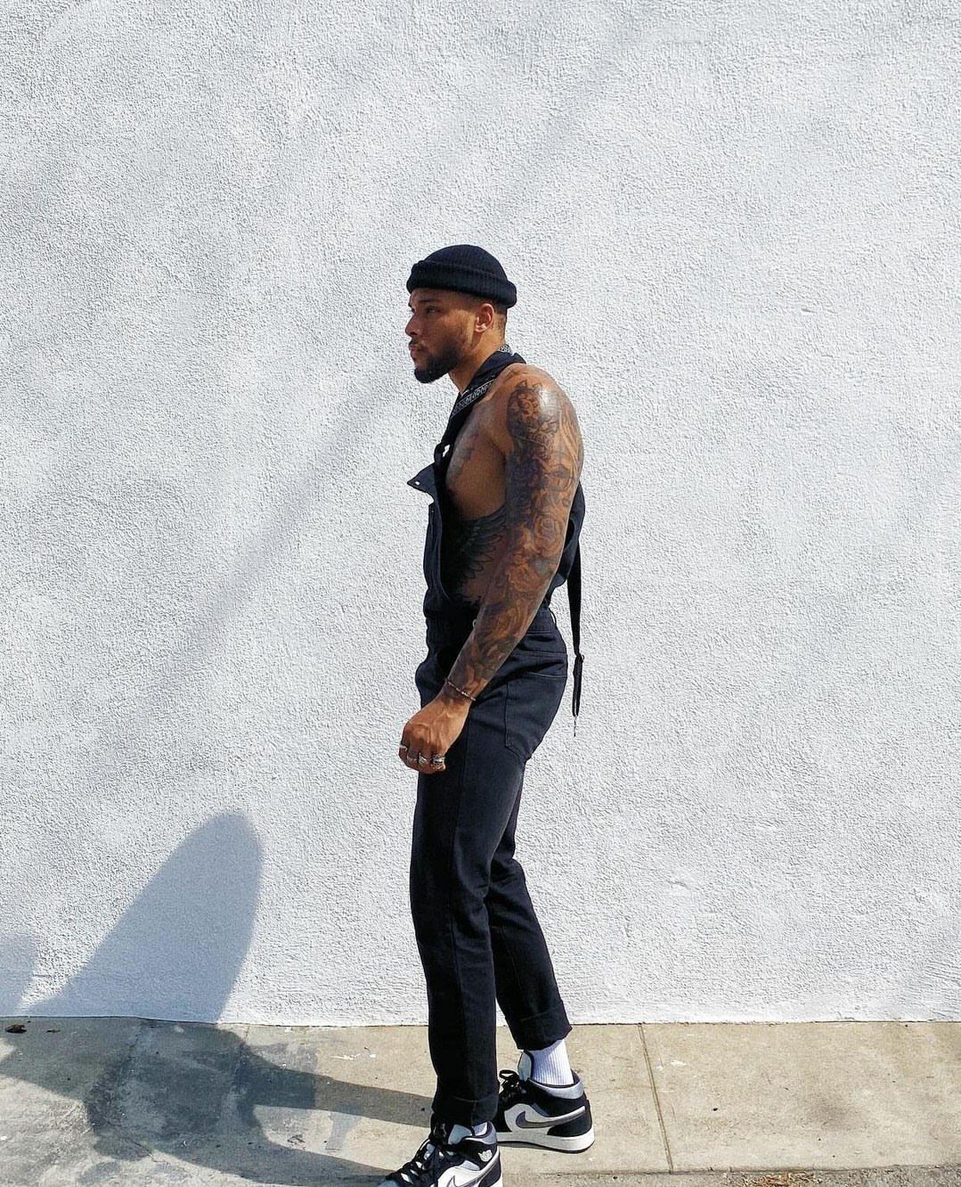 Man in black overalls with one strap loose and a black beanie.