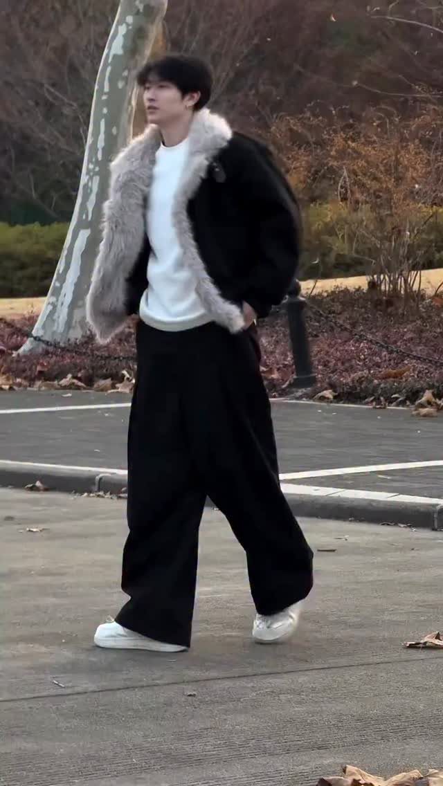Man wearing a black coat with fur collar and wide black trousers walking outdoors