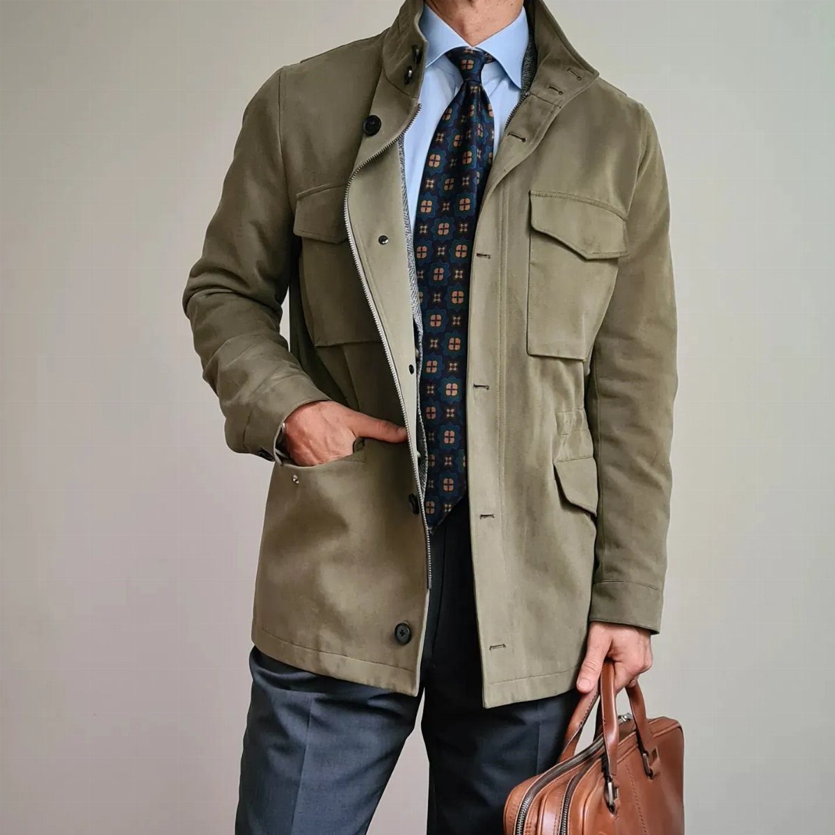 Man wearing an olive green field jacket with a tie and leather briefcase.