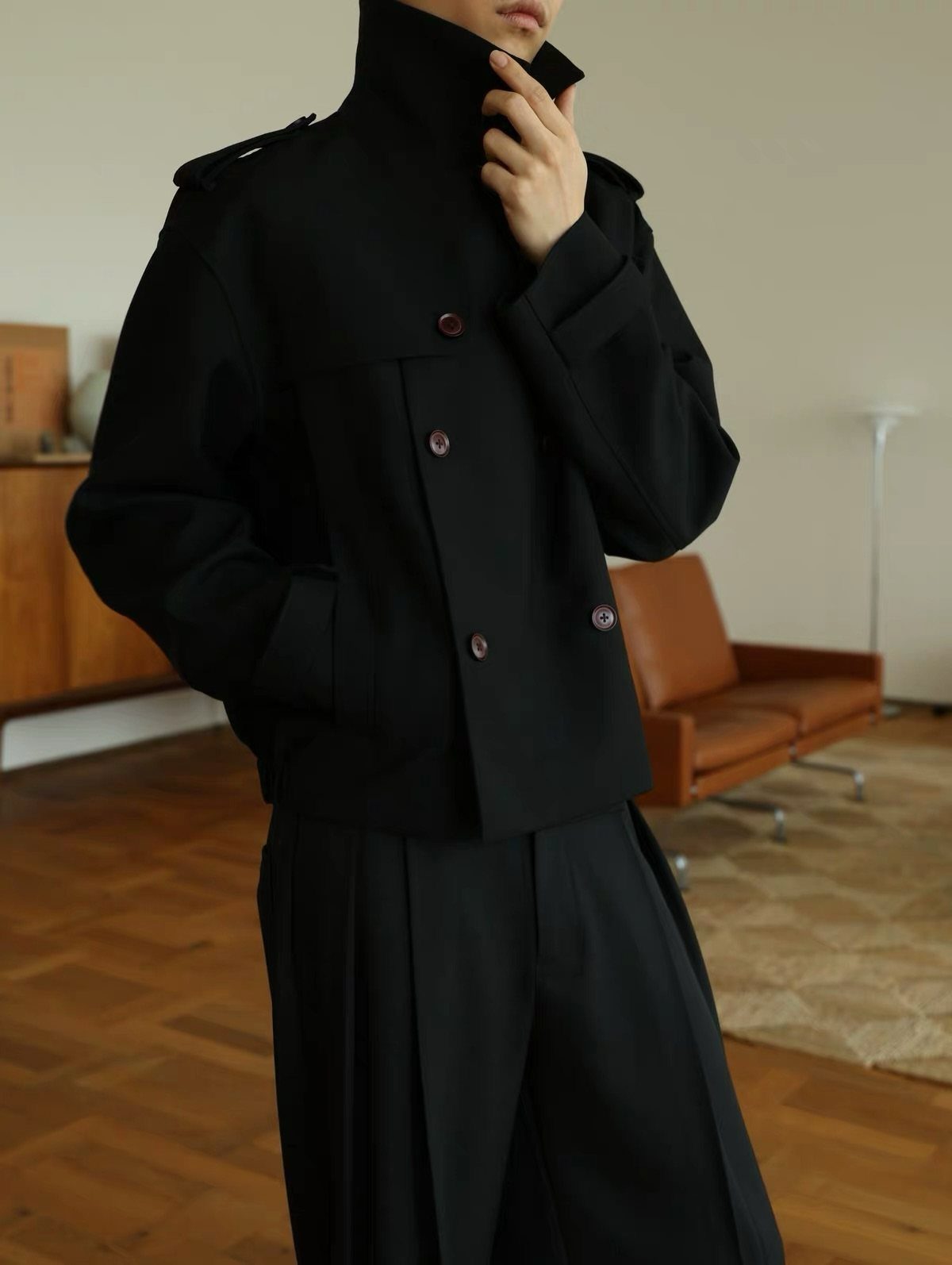 Person wearing a black short jacket and wide-leg trousers in a modern room.