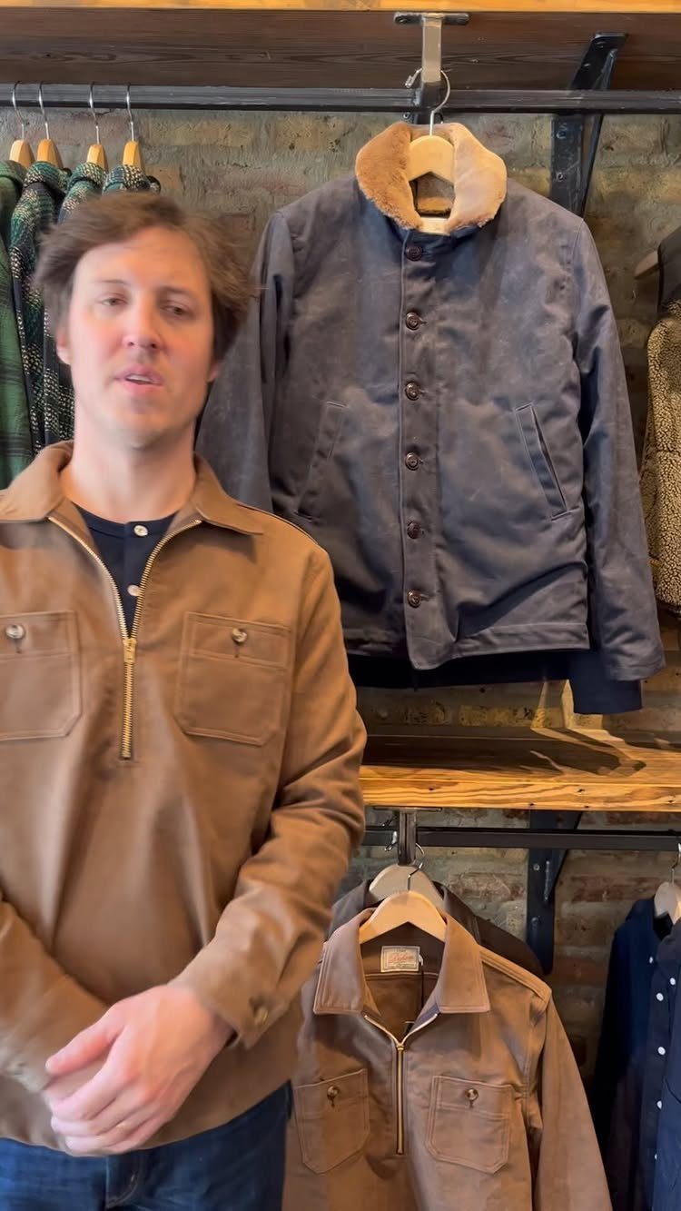 Man in tan quarter-zip jacket standing before a rack of men's outerwear.