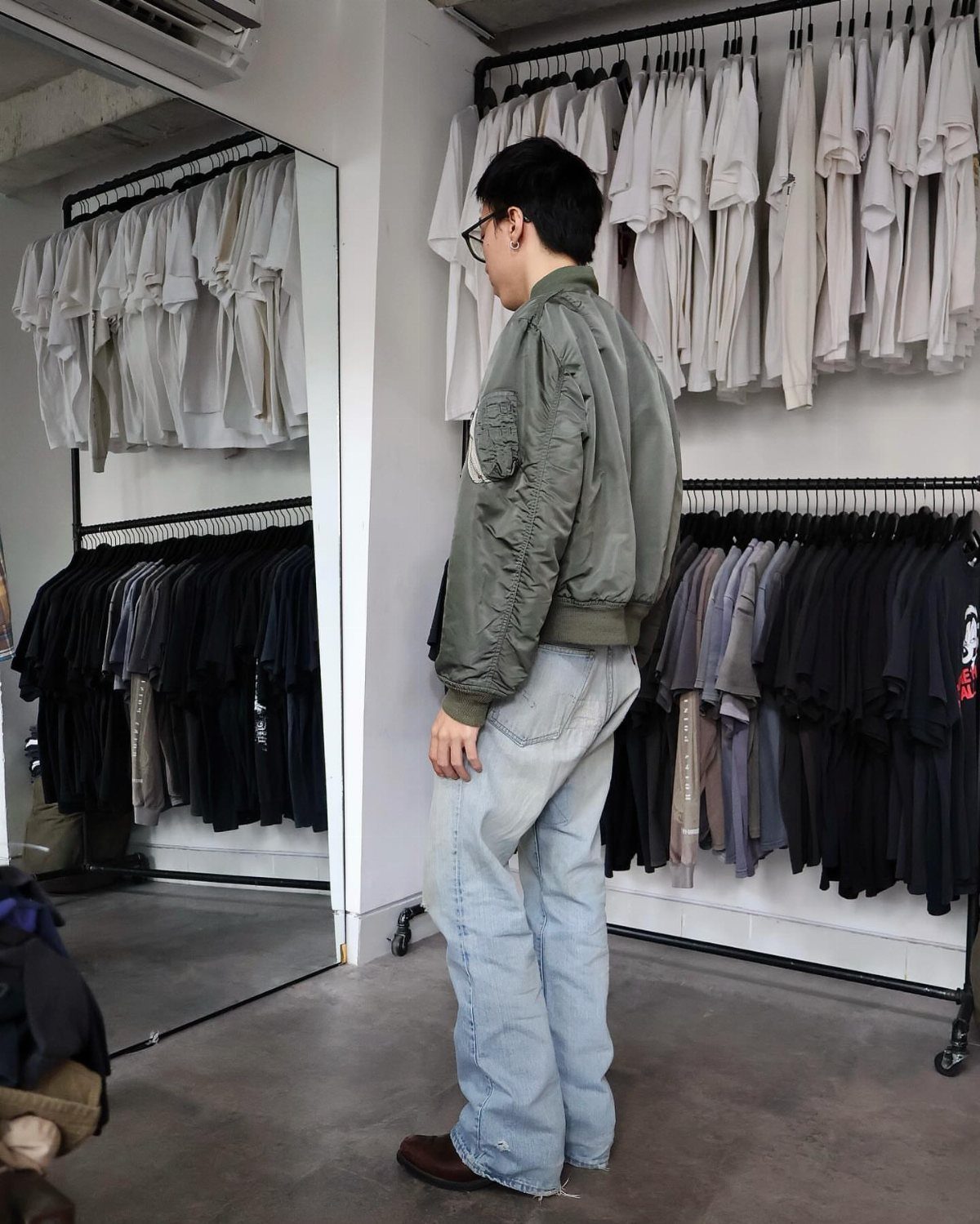 Person wearing an olive green bomber jacket and light blue wide-leg jeans in store